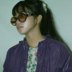 Stylish young woman wearing a purple jacket and oversized sunglasses, exuding a fashionable look.