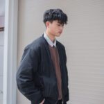 Young male model posing in fashionable attire outdoors with modern urban backdrop.