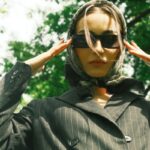 Stylish woman in headscarf and sunglasses posed outdoors in elegant fashion.