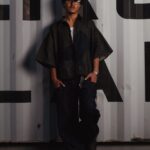 Casual portrait of a stylish man leaning against a container in dim light.