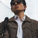 A fashionable young man wearing sunglasses and a jacket, exuding confidence. Urban setting.