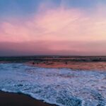 A tranquil scene of a Bali beach at sunset with pink and blue hues over the ocean.